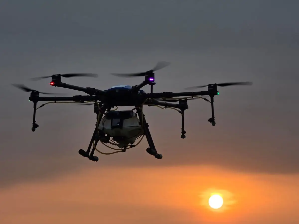 A crop-spraying drone flying against a sunset sky