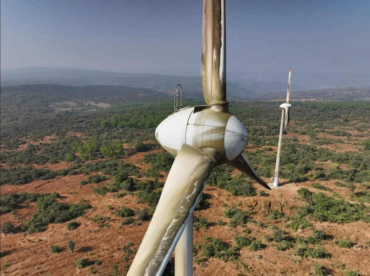 A wind turbine's hub and blades seen close up from a drone, a second turbine behind
